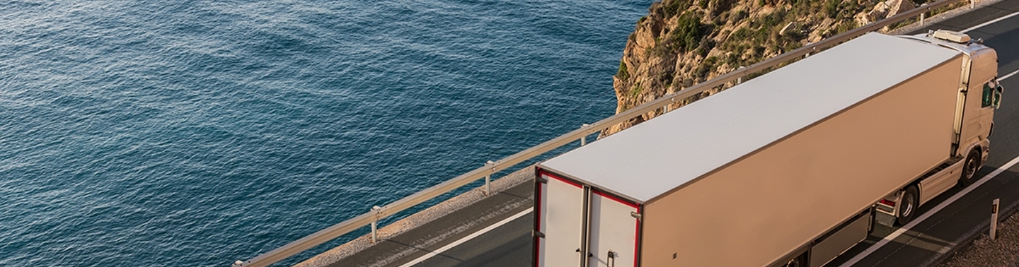 White semi truck driving on road next to ocean